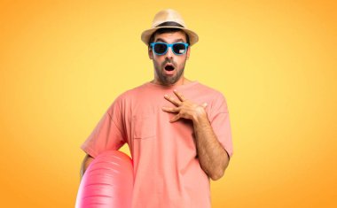 Yaz tatilinde şapkalı ve güneş gözlüklü adam doğru bakarken şaşırmış ve şok etmiştir. Turuncu arka planda etkileyici yüz hissi