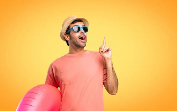 彼の夏休みに帽子とサングラスを持つ男が立って オレンジ色の背景に指を指差すアイデアを考えています — ストック写真
