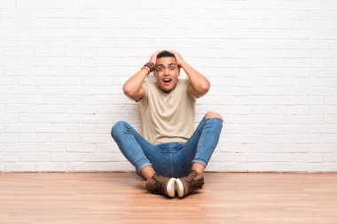 Genç bir adam yerde oturuyor ve yüzünde sürpriz bir ifade var.