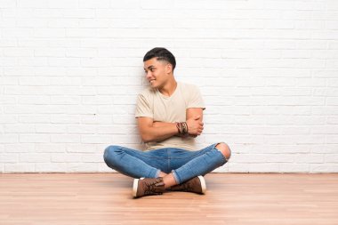 Genç adam yerde oturuyor, yan tarafa bakıyor.