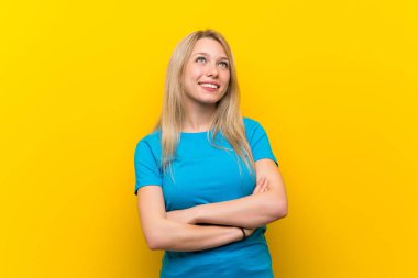 Sarı arka planda yaşayan genç sarışın kadın gülümserken yukarı bakıyor.