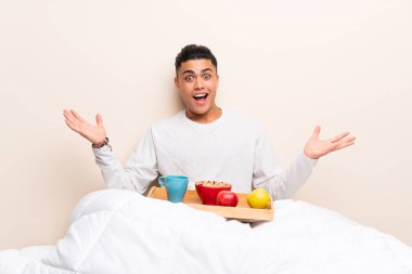 Sürpriz yüz ifadesi ile yatakta kahvaltı genç adam