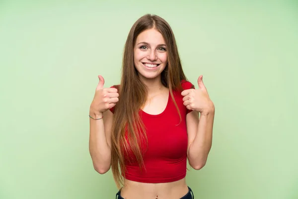 孤立した緑の壁の上に長い髪を持つ若い女性は 親指を上げるジェスチャーを与える — ストック写真