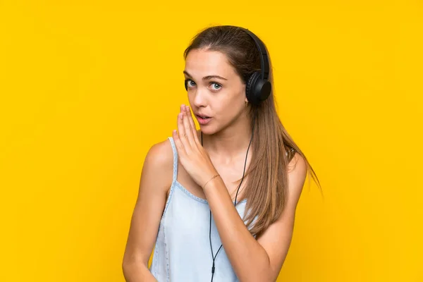 Mujer Joven Escuchando Música Sobre Una Pared Amarilla Aislada Susurrando —  Fotos de Stock