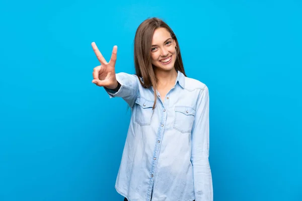 Jonge Vrouw Geïsoleerde Blauwe Achtergrond Glimlachen Tonen Overwinning Teken — Stockfoto