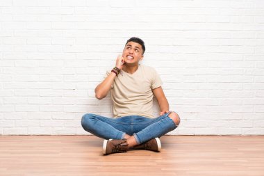 Genç adam yerde oturmuş bir fikir düşünüyor.