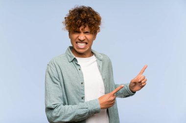 Izole mavi duvar üzerinde genç afro-amerikan adam korkmuş ve yan işaret