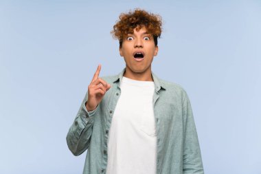 Izole mavi duvar üzerinde genç afro-amerikan adam işaret ve şaşırttı