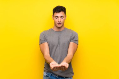 Bir reklam eklemek için avuç üzerinde copyspace hayali tutan izole sarı duvar üzerinde Yakışıklı adam