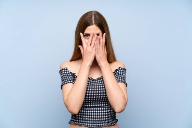 Gözleri kaplayan ve parmaklardan bakan izole mavi arka plan üzerinde genç kadın