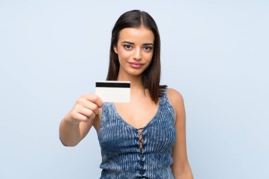 Bir kredi kartı tutan izole mavi duvar üzerinde genç kadın