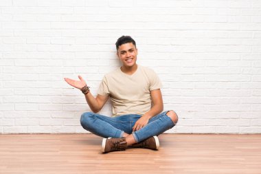 Genç adam avuç üzerinde hayali copyspace tutarak katta oturan