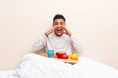 Yatakta kahvaltı eden genç adam ağzı tamamen açık diye bağırıyor