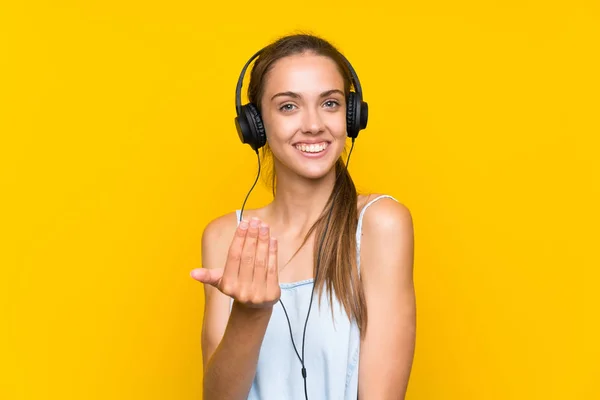 Young Woman Listening Music Isolated Yellow Wall Inviting Come Hand — Stock Photo, Image