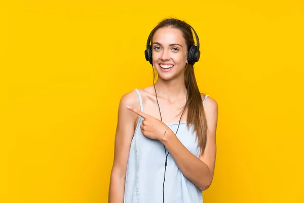 Mujer Joven Escuchando Música Sobre Una Pared Amarilla Aislada Apuntando —  Fotos de Stock