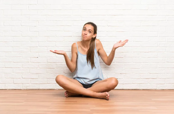 Young woman sitting on the floor having doubts with confuse face expression