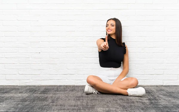 Mujer Joven Bonita Sentada Suelo Mostrando Levantando Dedo —  Fotos de Stock