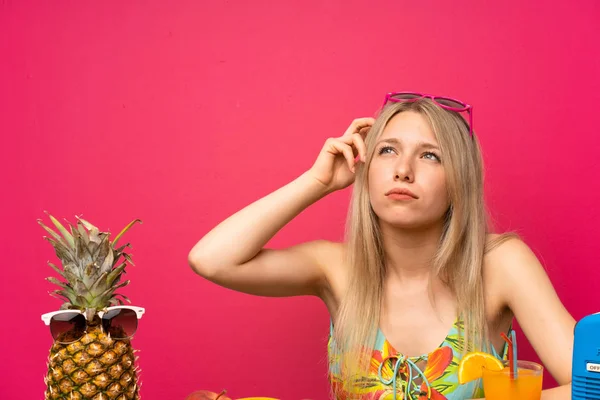 疑いを持ち 顔の表情を混乱させる果物の多くを持つ若いブロンドの女性 — ストック写真