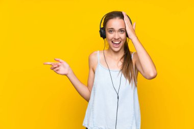 İzole sarı duvar üzerinde müzik dinleyen genç kadın şaşırttı ve yan parmak işaret