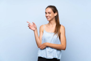 İzole edilmiş mavi arka planda genç bir kadın, parmağını yana doğru gösteriyor.