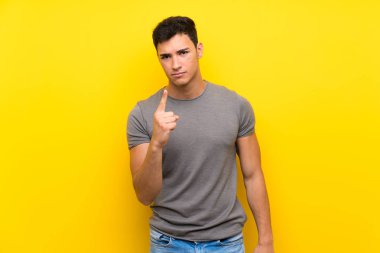 Izole sarı duvar üzerinde Yakışıklı adam sinirli ve ön işaret