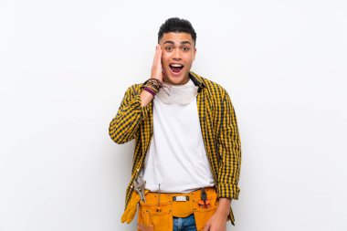 Sürpriz ve şok yüz ifadesi ile izole beyaz duvar üzerinde genç elektrikçi adam