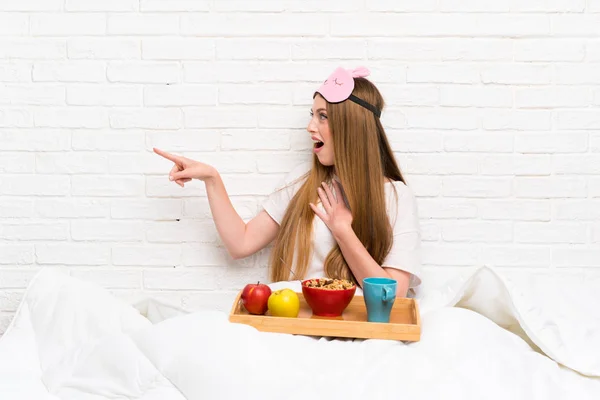 Young woman in dressing gown with breakfast pointing finger to the side