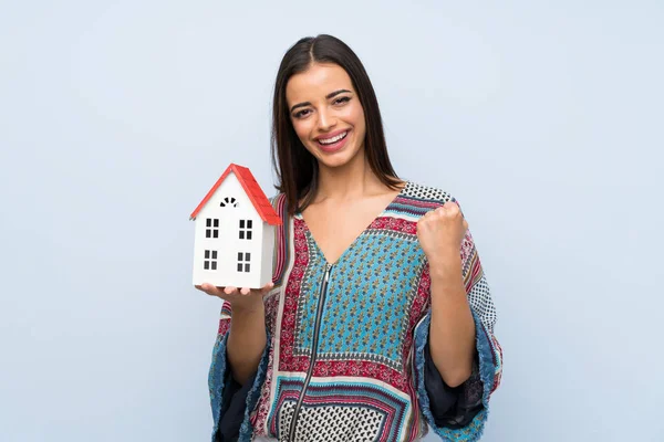 Jonge Vrouw Geïsoleerde Blauwe Muur Houden Een Klein Huis — Stockfoto