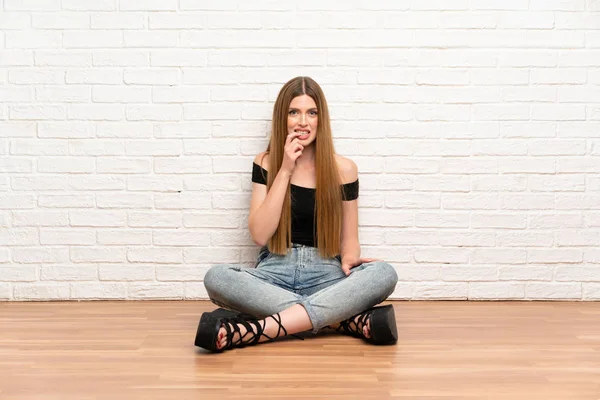 Young woman sitting on the floor nervous and scared