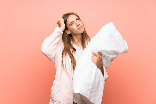 Young woman in dressing gown over pink wall having doubts and with confuse face expression