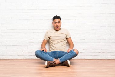 Genç bir adam yerde oturuyor ve yüzünde sürpriz bir ifade var.