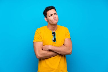 Omuzları kaldırırken mavi arka plan üzerinde yakışıklı adam şüphe jest yapma