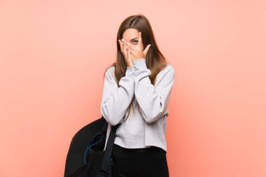 Gözleri kaplayan izole pembe arka plan üzerinde genç spor kadın ve parmaklardan bakarak