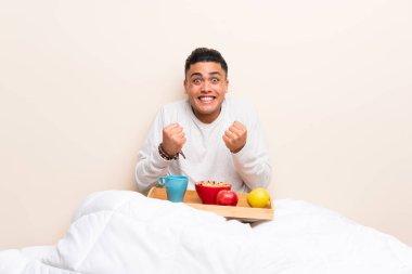 Genç adam yatakta zafer kutluyor kahvaltı yapıyor