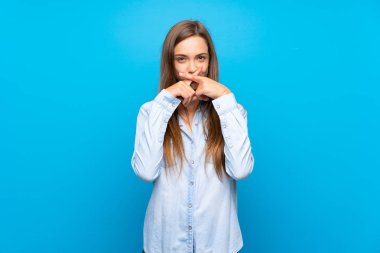 İzole edilmiş mavi arka planda genç bir kadın sessizlik işareti gösteriyor.