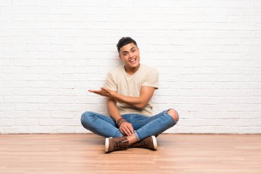 Genç adam yere oturmuş, davet edildiği için ellerini yana açıyor.