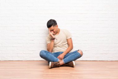 Genç adam yerde oturmuş gülüyor.