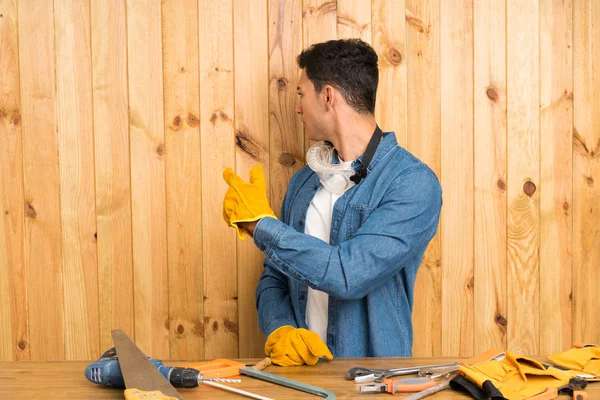 Craftsmen man over wood background pointing back with the index finger