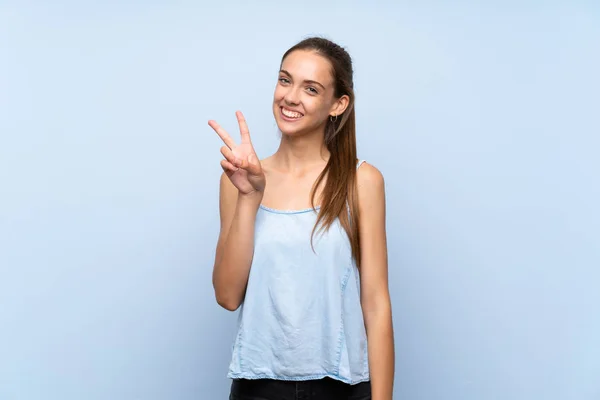 Молода Жінка Над Ізольованим Синім Тлом Посміхається Показує Знак Перемоги — стокове фото