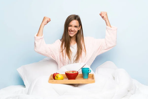 Young woman in dressing gown with breakfast celebrating a victory