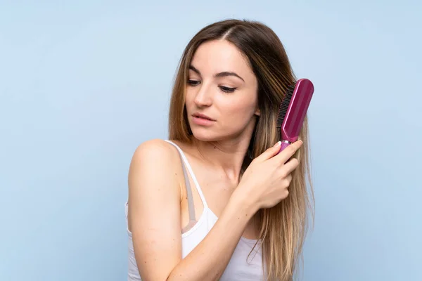 Mujer Joven Sobre Fondo Azul Aislado Con Peine Pelo —  Fotos de Stock