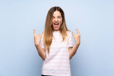 Izole mavi arka plan üzerinde rock jest yapma genç kadın