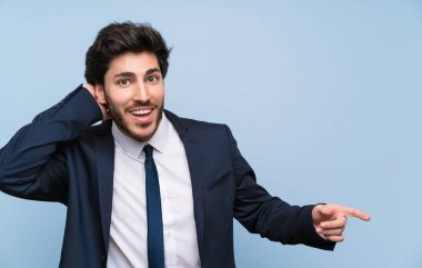 İzole mavi duvar üzerinde işadamı şaşırttı ve yan parmak işaret