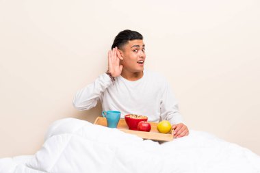 Yatakta kahvaltı olan genç adam bir şeyler dinleyerek