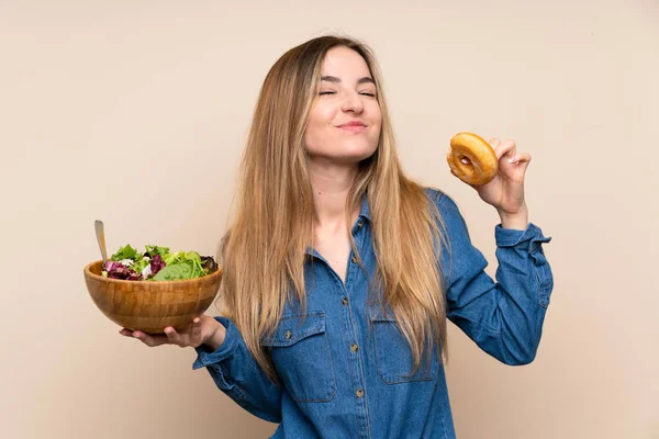 Junge Frau Mit Salat Über Isoliertem Hintergrund Und Einem Donut — Stockfoto