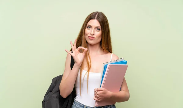 年轻的学生妇女在孤立的绿色背景显示一个确定的标志用手指 — 图库照片