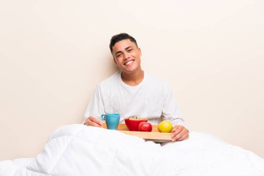 Yatakta gülerek kahvaltı alan genç adam