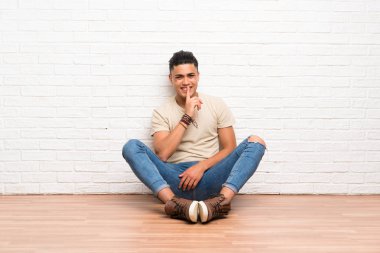 Yerde oturan genç adam sessizlik jesti yapıyor