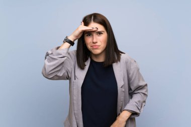 Bir şey bakmak için elle uzak görünümlü izole mavi duvar üzerinde genç kadın