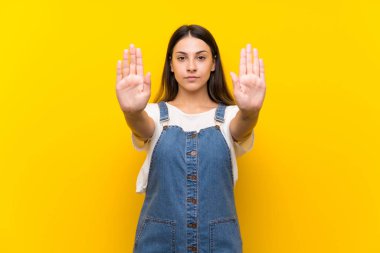 Izole sarı arka plan üzerinde dungarees genç kadın stop jest yapma ve hayal kırıklığına